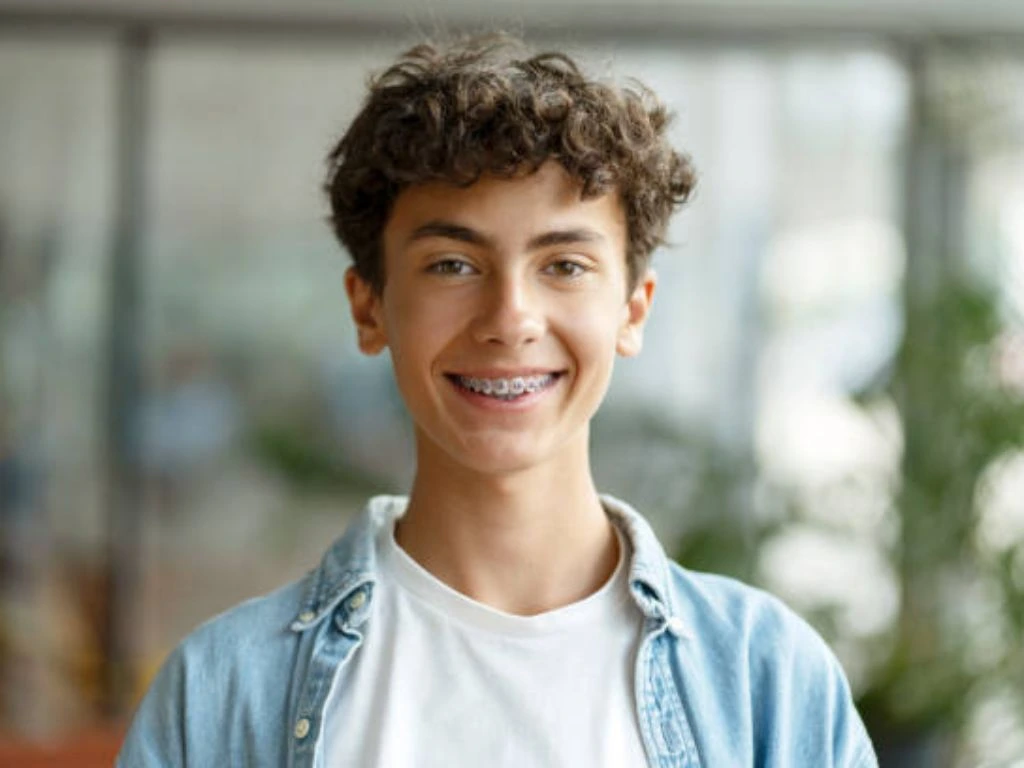 A 16 year old boy smiling while wearing traditional braces, showcasing orthodontic treatment for teenagers